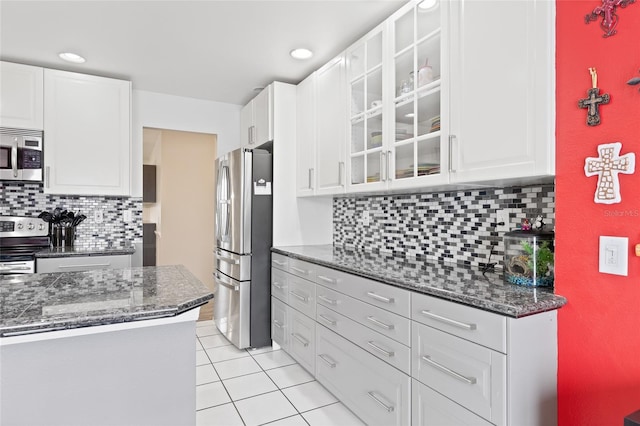 kitchen with white cabinets, light tile patterned floors, tasteful backsplash, appliances with stainless steel finishes, and dark stone countertops