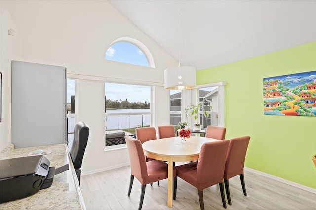 dining area featuring baseboards, a water view, high vaulted ceiling, and light wood-style flooring