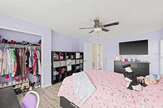bedroom featuring a closet, a textured ceiling, visible vents, ceiling fan, and wood finished floors