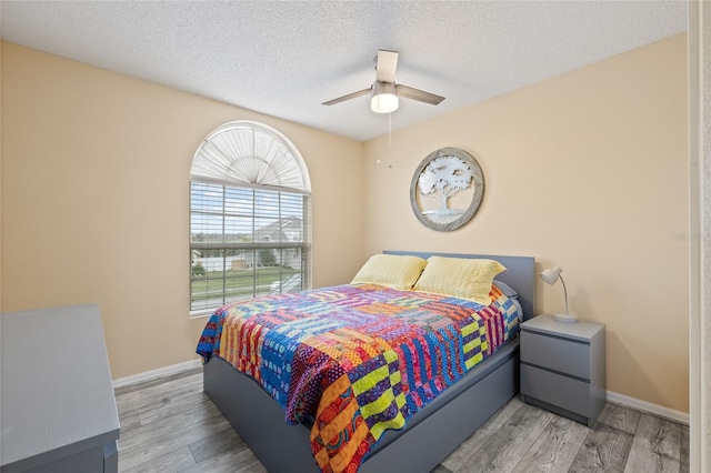 bedroom with baseboards, a textured ceiling, ceiling fan, and light wood finished floors