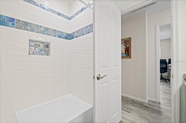 bathroom with baseboards, visible vents, wood finished floors, and bathing tub / shower combination
