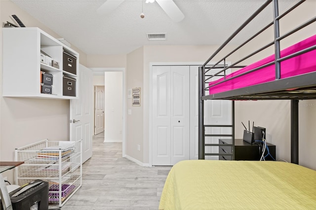 bedroom with baseboards, a textured ceiling, visible vents, a closet, and wood finished floors