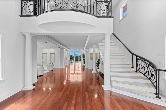 foyer entrance featuring a chandelier, wood-type flooring, ornate columns, and a high ceiling