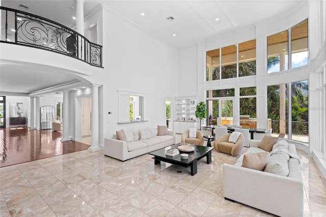 living room featuring a towering ceiling, ornate columns, a wealth of natural light, and ornamental molding