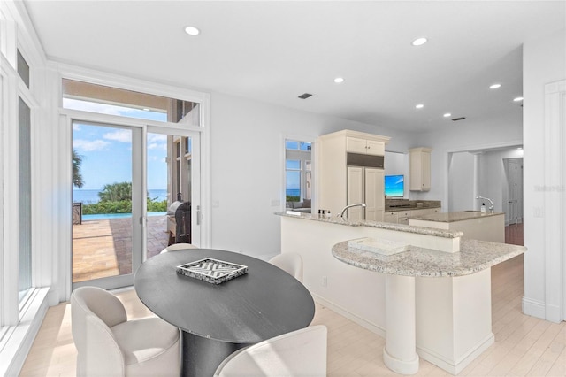 kitchen featuring light stone countertops, light wood-type flooring, paneled refrigerator, a kitchen island with sink, and sink