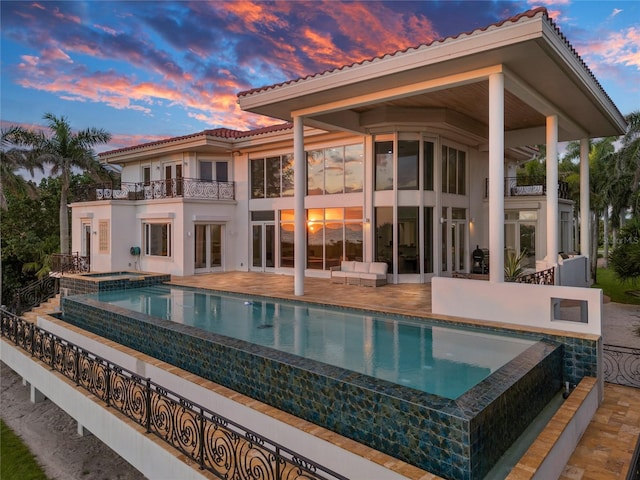 back house at dusk featuring a patio and a balcony