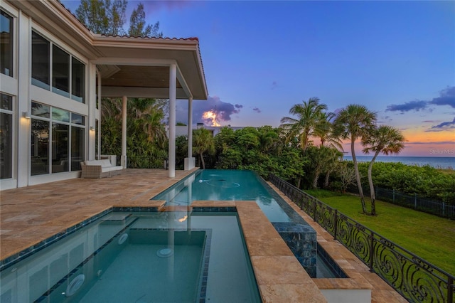 pool at dusk featuring an in ground hot tub, a patio, and a lawn