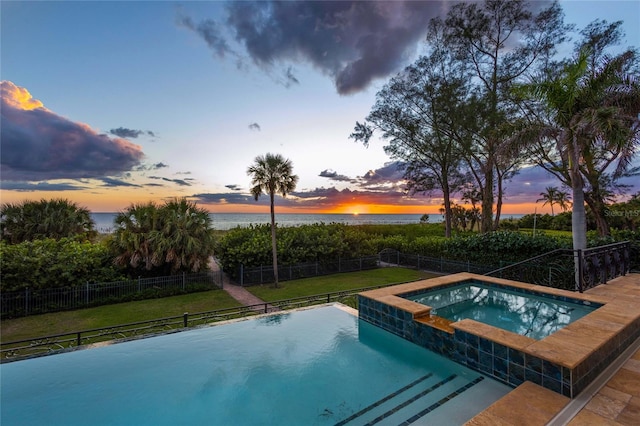 pool at dusk featuring an in ground hot tub, a yard, and a water view