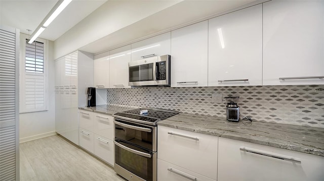 kitchen featuring backsplash, appliances with stainless steel finishes, light stone countertops, white cabinets, and light hardwood / wood-style flooring