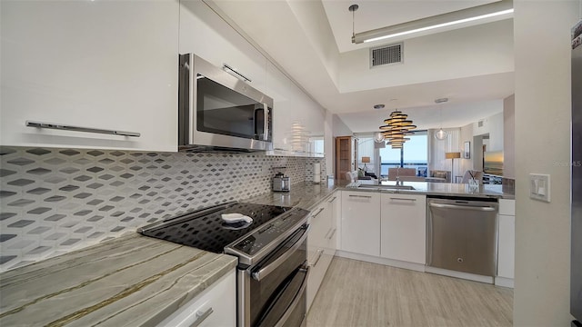 kitchen with tasteful backsplash, appliances with stainless steel finishes, hanging light fixtures, sink, and white cabinets