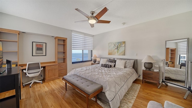 bedroom featuring built in desk, ceiling fan, a textured ceiling, and light hardwood / wood-style flooring