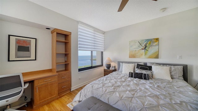 bedroom with light wood-type flooring, a textured ceiling, built in desk, and ceiling fan