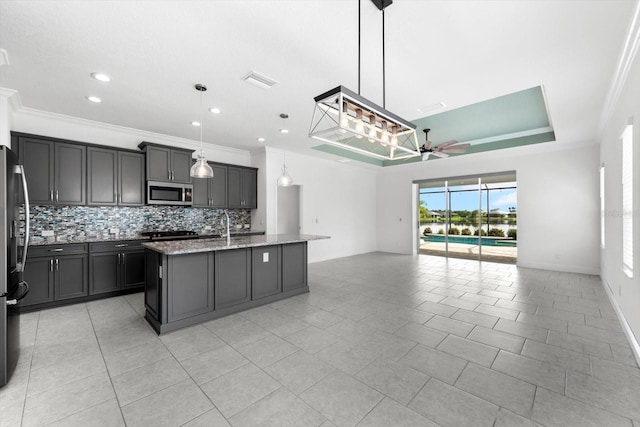 kitchen featuring ceiling fan, light stone countertops, stainless steel appliances, an island with sink, and pendant lighting