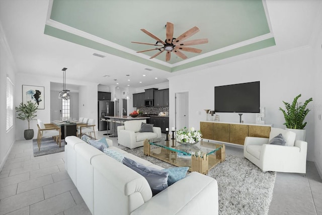 living room with a raised ceiling, ceiling fan, and light tile patterned flooring