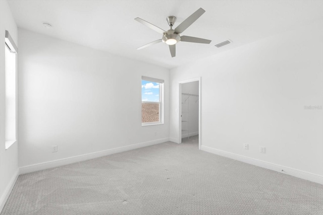 unfurnished bedroom featuring ceiling fan, a closet, light carpet, and a spacious closet