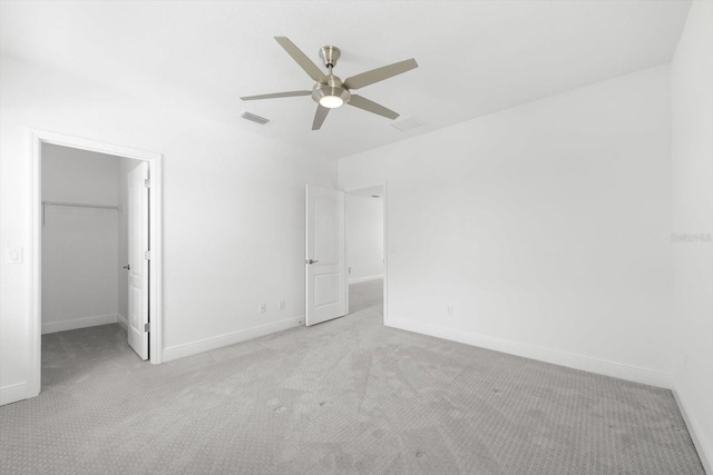 unfurnished bedroom featuring a walk in closet, ceiling fan, a closet, and light carpet