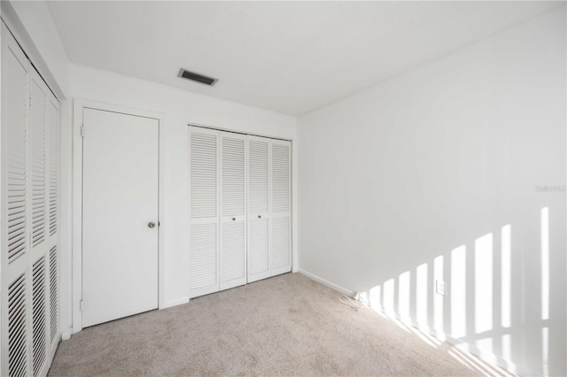 unfurnished bedroom featuring light colored carpet and two closets