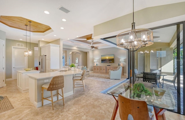 kitchen with a kitchen island with sink, a kitchen breakfast bar, pendant lighting, white cabinetry, and high quality fridge