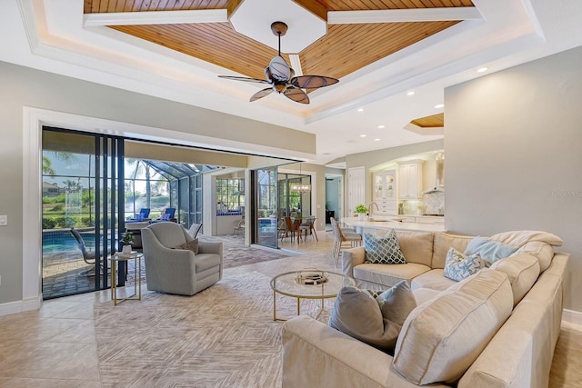 tiled living room featuring wood ceiling, sink, ceiling fan, and a raised ceiling