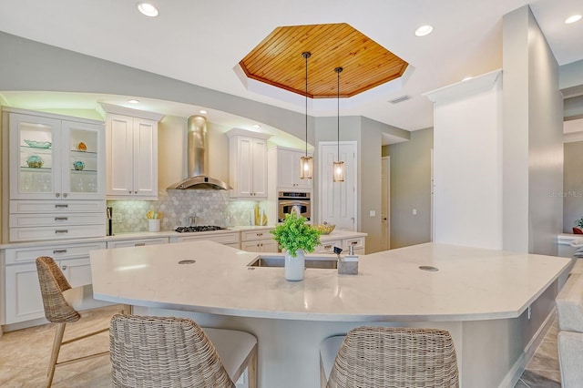 kitchen with tasteful backsplash, wall chimney range hood, white cabinetry, appliances with stainless steel finishes, and decorative light fixtures