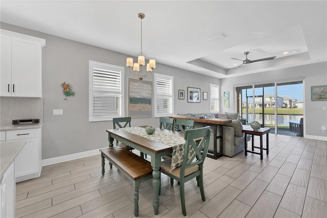 dining area featuring a raised ceiling, a water view, and ceiling fan with notable chandelier