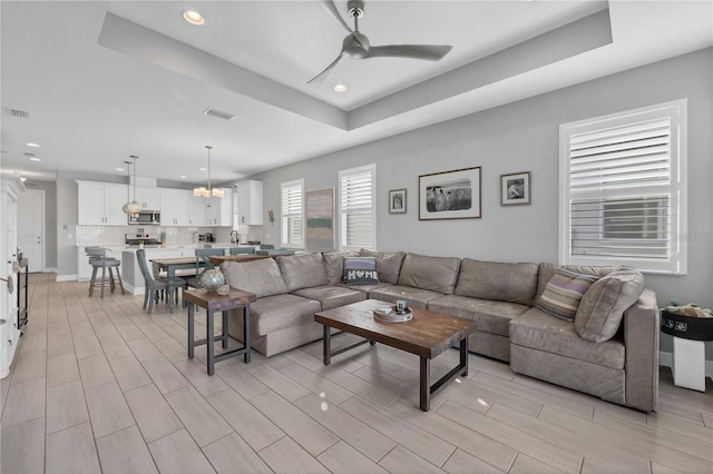 living room featuring a raised ceiling and ceiling fan with notable chandelier