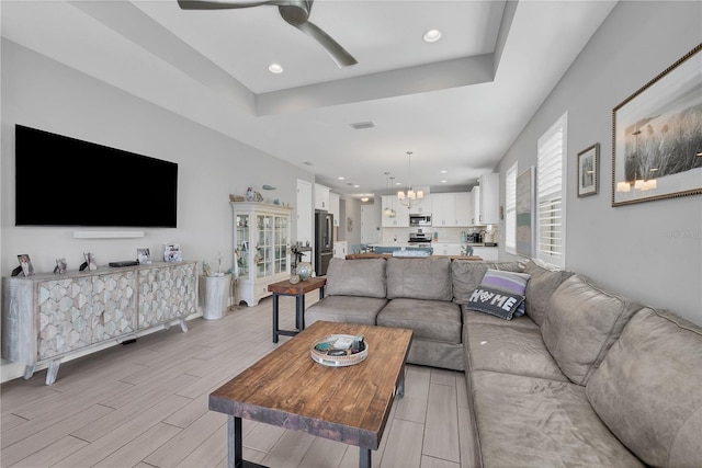 living room featuring ceiling fan with notable chandelier and a tray ceiling