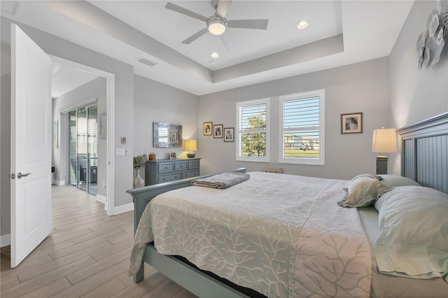 bedroom featuring a raised ceiling, light wood-type flooring, access to exterior, and ceiling fan