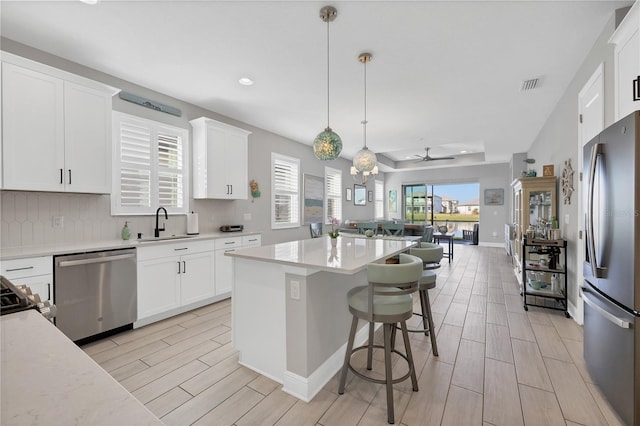 kitchen featuring decorative light fixtures, stainless steel appliances, white cabinetry, and a center island