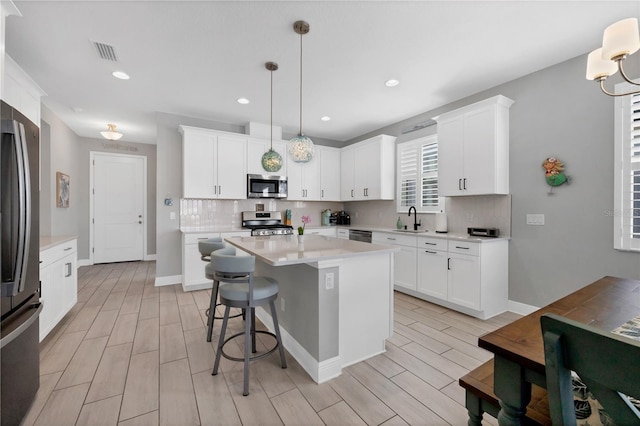 kitchen with white cabinetry, stainless steel appliances, a center island, decorative light fixtures, and sink