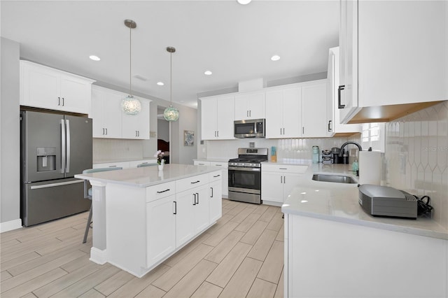 kitchen with hanging light fixtures, a kitchen island, sink, appliances with stainless steel finishes, and white cabinets