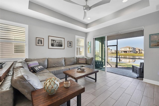 living room featuring a tray ceiling, a water view, and ceiling fan