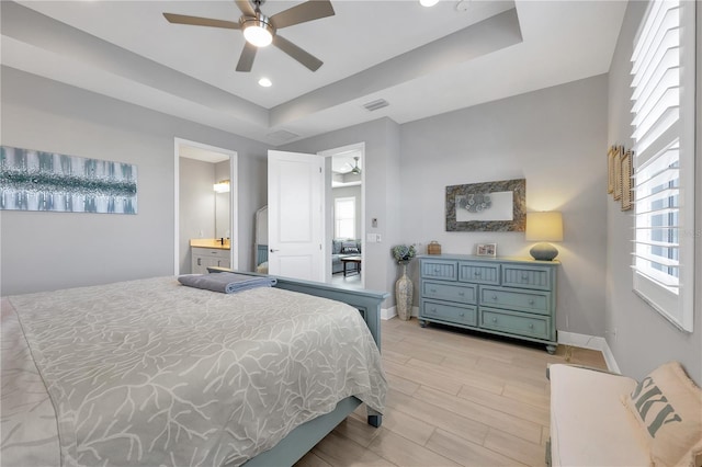 bedroom featuring a tray ceiling, light hardwood / wood-style flooring, connected bathroom, and ceiling fan