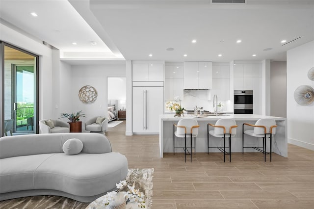 kitchen with white cabinets, an island with sink, a kitchen breakfast bar, double oven, and light hardwood / wood-style flooring