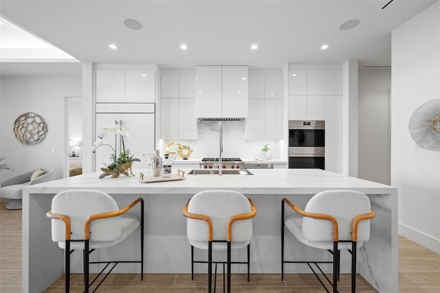 kitchen with white cabinets, a center island with sink, and stainless steel double oven