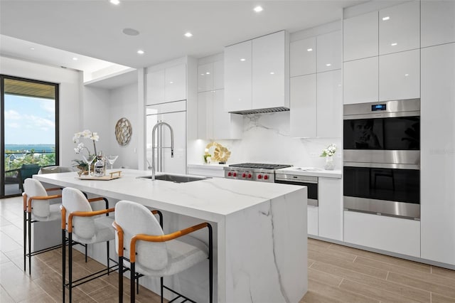 kitchen featuring a center island with sink, white cabinets, sink, a kitchen breakfast bar, and double oven