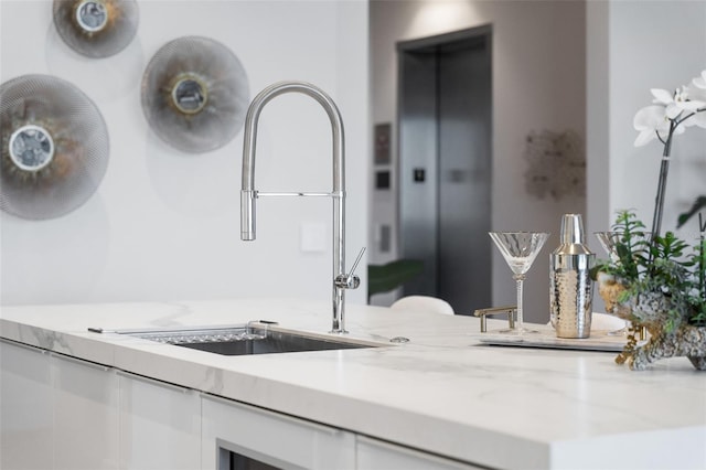 kitchen with light stone countertops, sink, and white cabinets