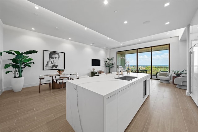 kitchen featuring light stone counters, sink, an island with sink, light hardwood / wood-style floors, and white cabinets