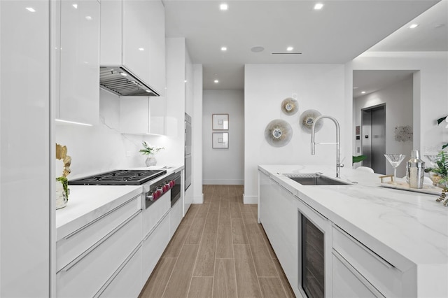 kitchen featuring beverage cooler, white cabinetry, sink, and light stone countertops