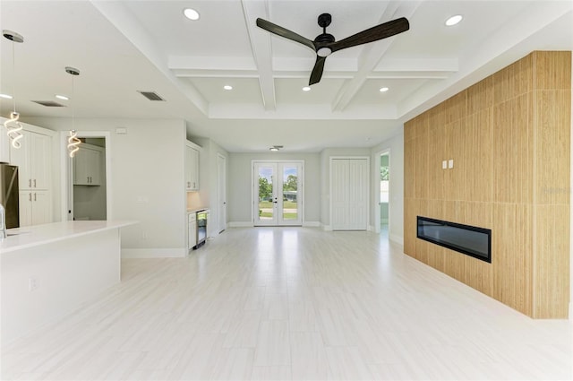 unfurnished living room featuring french doors, coffered ceiling, a large fireplace, beamed ceiling, and ceiling fan