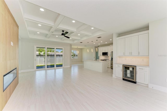 unfurnished living room with sink, beam ceiling, wine cooler, coffered ceiling, and a fireplace