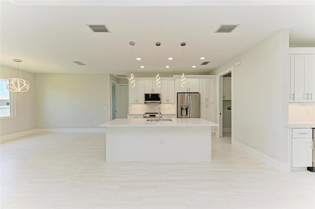 kitchen with stainless steel appliances, white cabinetry, an island with sink, and decorative light fixtures