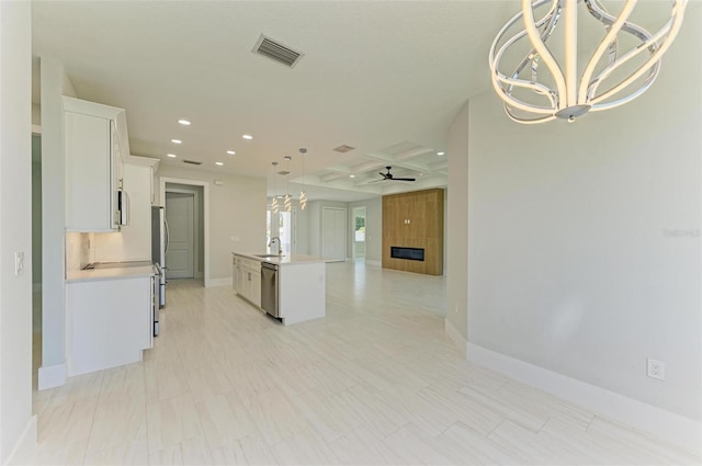 kitchen featuring stainless steel appliances, beam ceiling, coffered ceiling, an island with sink, and white cabinets