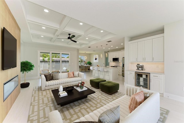 living room featuring coffered ceiling, a fireplace, beverage cooler, and beamed ceiling