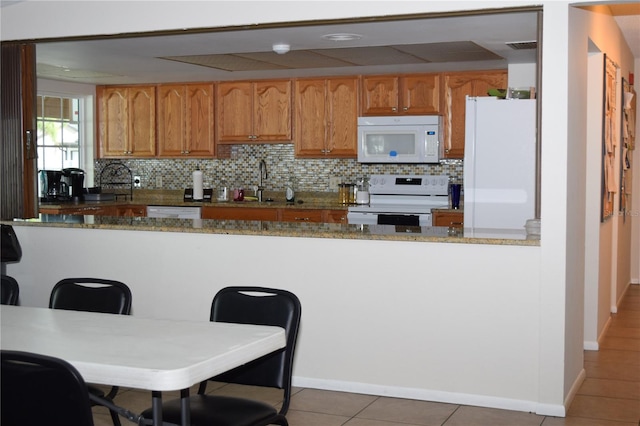 kitchen featuring a kitchen breakfast bar, tile patterned floors, stone countertops, white appliances, and decorative backsplash