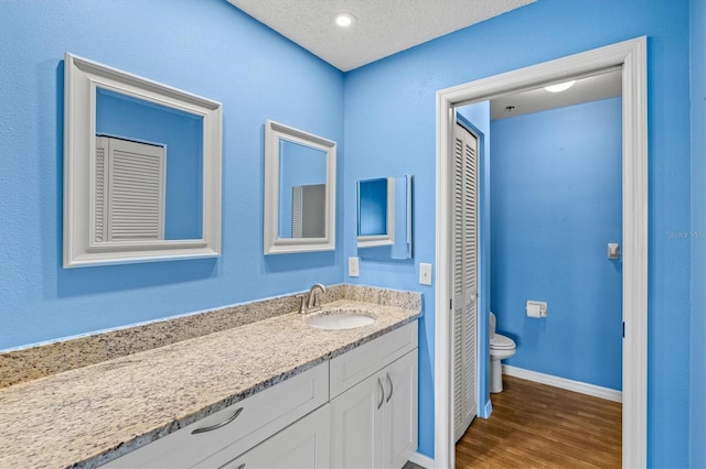 bathroom with hardwood / wood-style flooring, vanity, a textured ceiling, and toilet