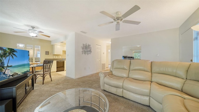 living room featuring ceiling fan, light colored carpet, baseboards, and a textured ceiling