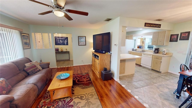 living room with radiator heating unit, ceiling fan, sink, and light wood-type flooring