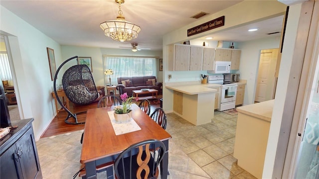 kitchen with hanging light fixtures, kitchen peninsula, white appliances, light tile patterned flooring, and ceiling fan with notable chandelier