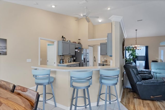 kitchen featuring ceiling fan with notable chandelier, a breakfast bar, gray cabinetry, and stainless steel fridge